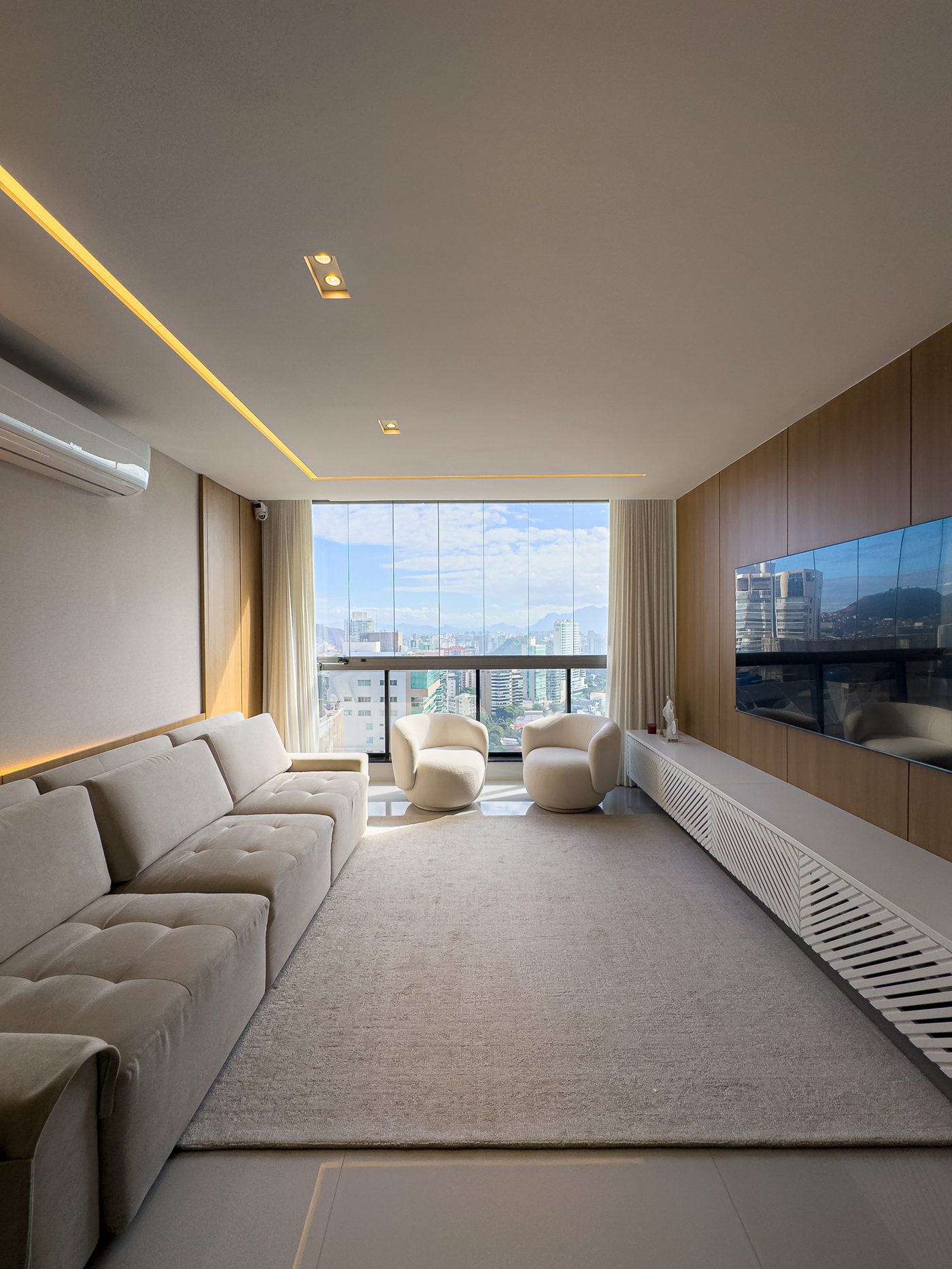 Sala ampla com sofá claro e varanda envidraçada com vista para a cidade